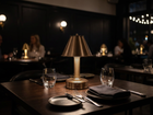 A cordless mini brass table lamp from modern lantern sits on a dark wooden restaurant table