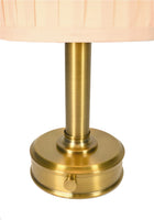 Close-up of a cordless table lamp with a round brushed brass base and a pleated light beige fabric shade by modern lantern