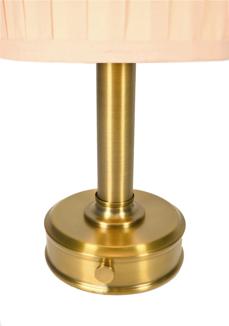 Close-up of a cordless table lamp with a round brushed brass base and a pleated light beige fabric shade by modern lantern