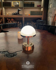 Mini cordless lamp in antique brass with frosted glass, illuminating a dining table in a cozy setting.