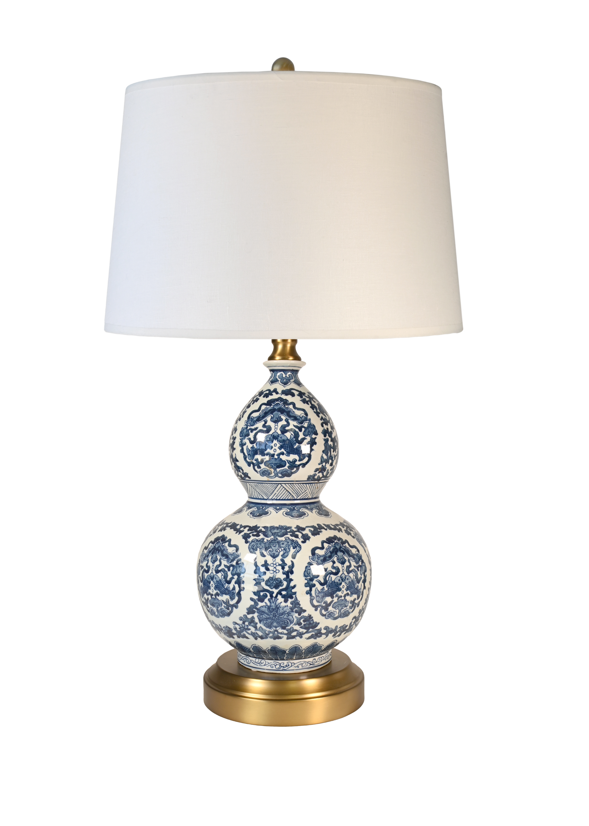 A cordless table lamp with a white drum shade, a blue and white porcelain gourd-shaped ceramic base, and a brass-finished metal neck and circular base.