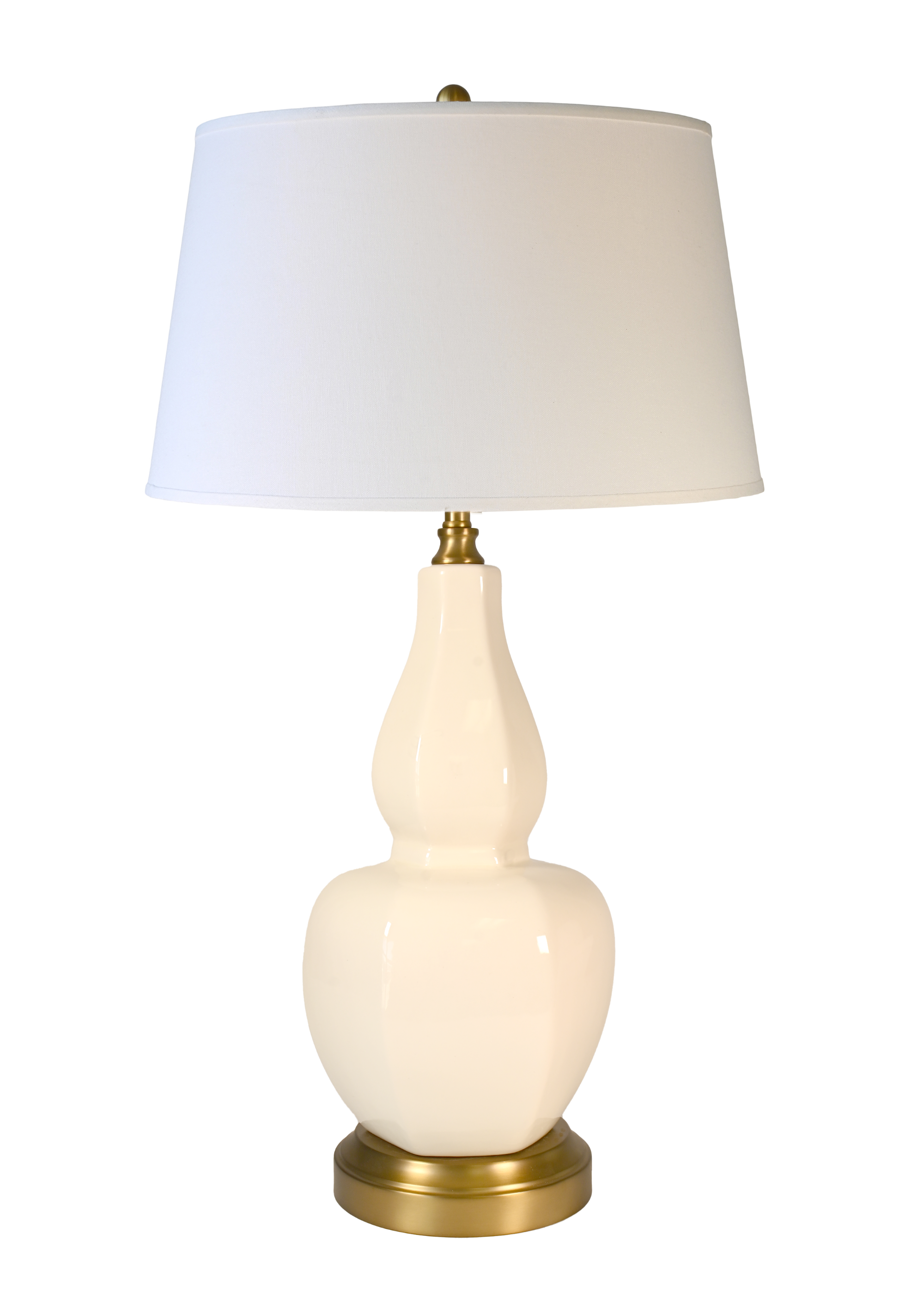 A cordless table lamp with a glossy cream-colored ceramic gourd-shaped base, an off white fabric drum shade, and a brass-finished metal accents at the neck and bottom.