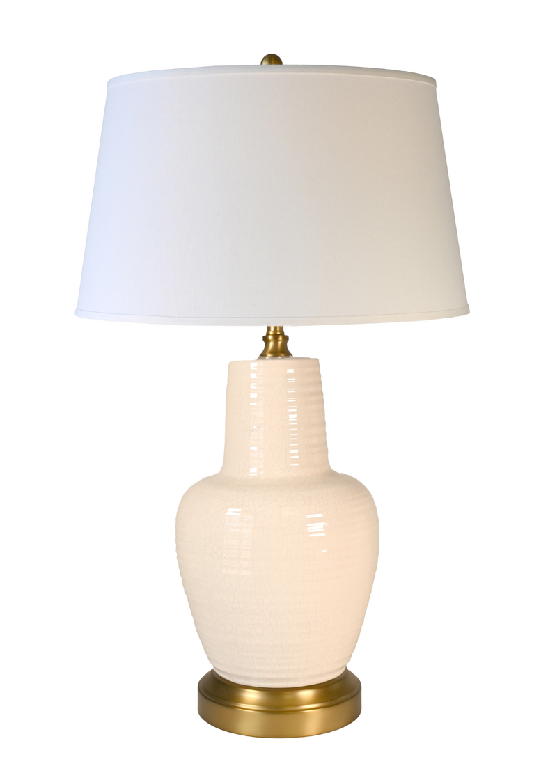 A cordless table lamp with an ivory ceramic ribbed vase base, an off white fabric drum shade, and a brass-finished metal neck and circular base.