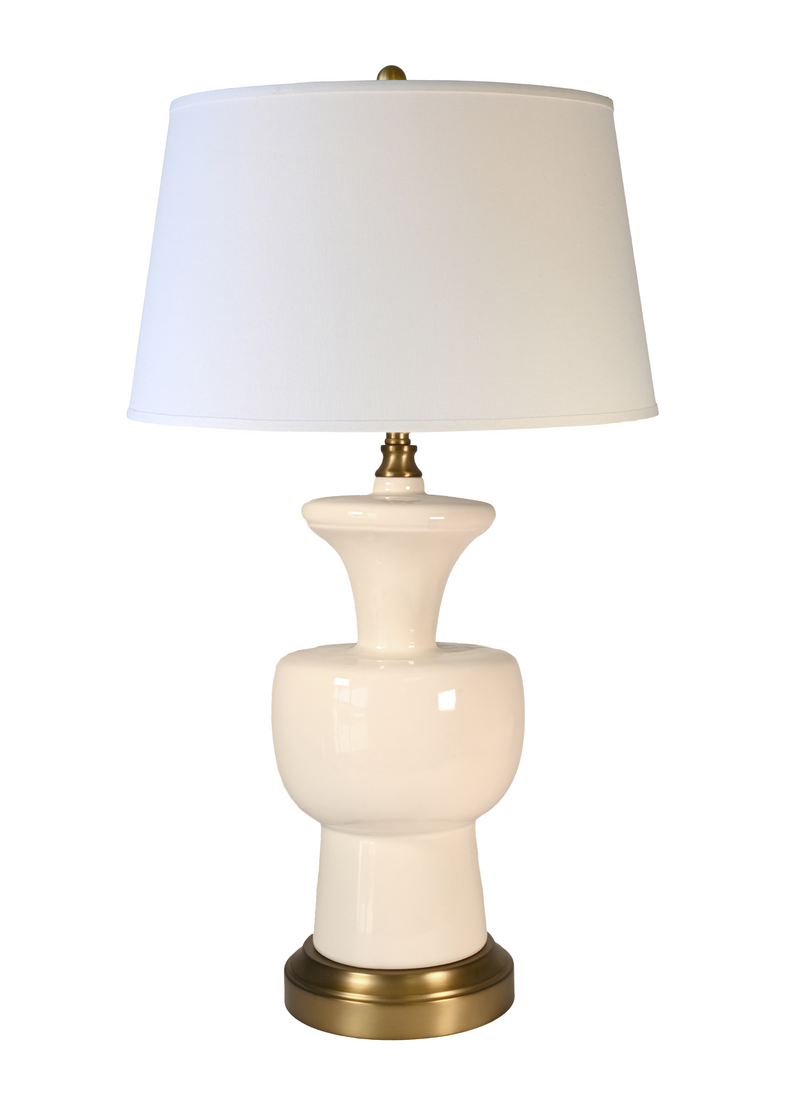 A cordless table lamp with a glossy cream ceramic vase-shaped base, an off-white fabric drum shade, and a polished brass-finished metal top and bottom trim