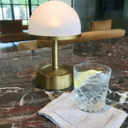 Mini cordless lamp in antique brass with alabaster frosted glass on a marble table beside a glass .